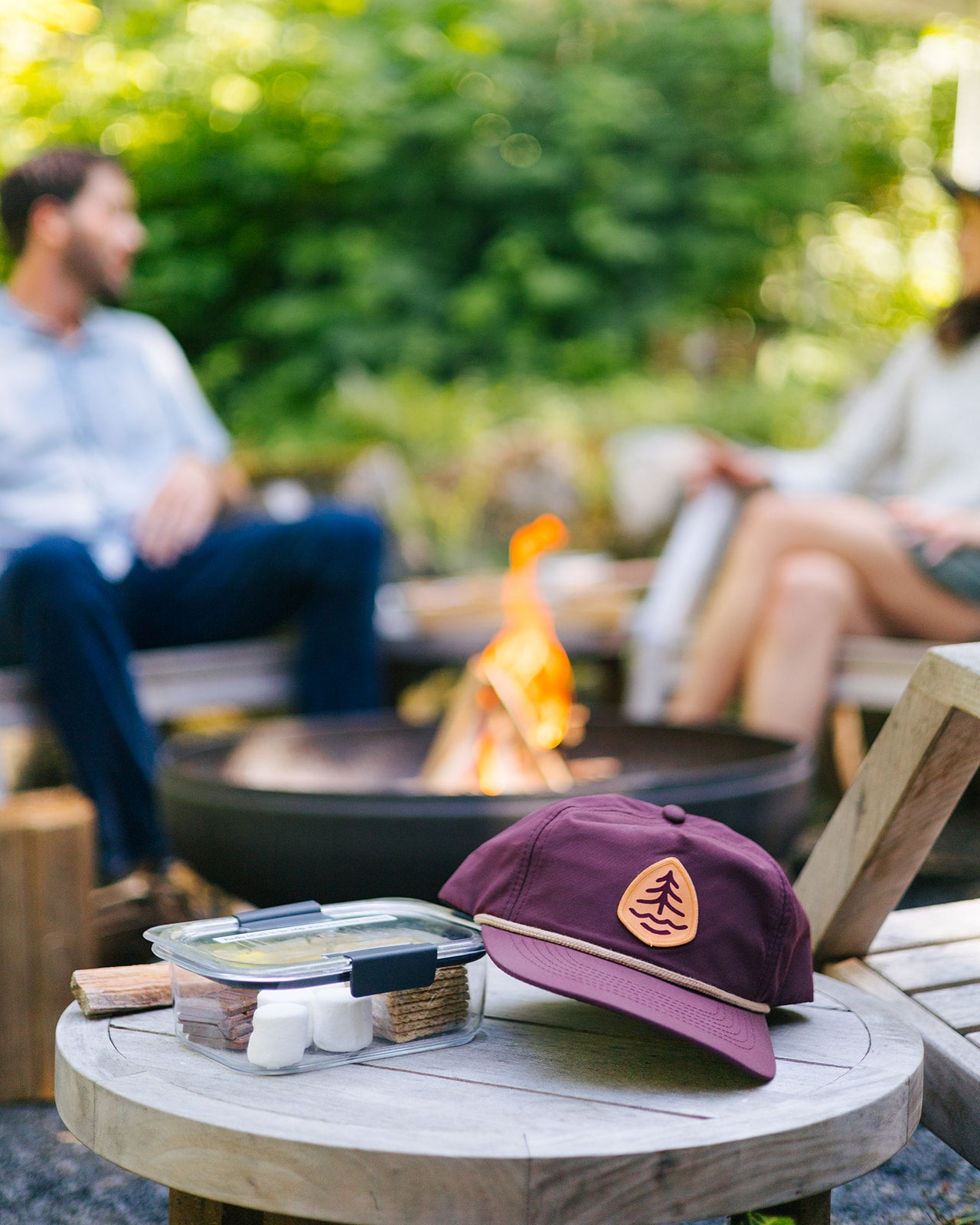 Treehouse Point Hat with couple lounging by firepit behind it